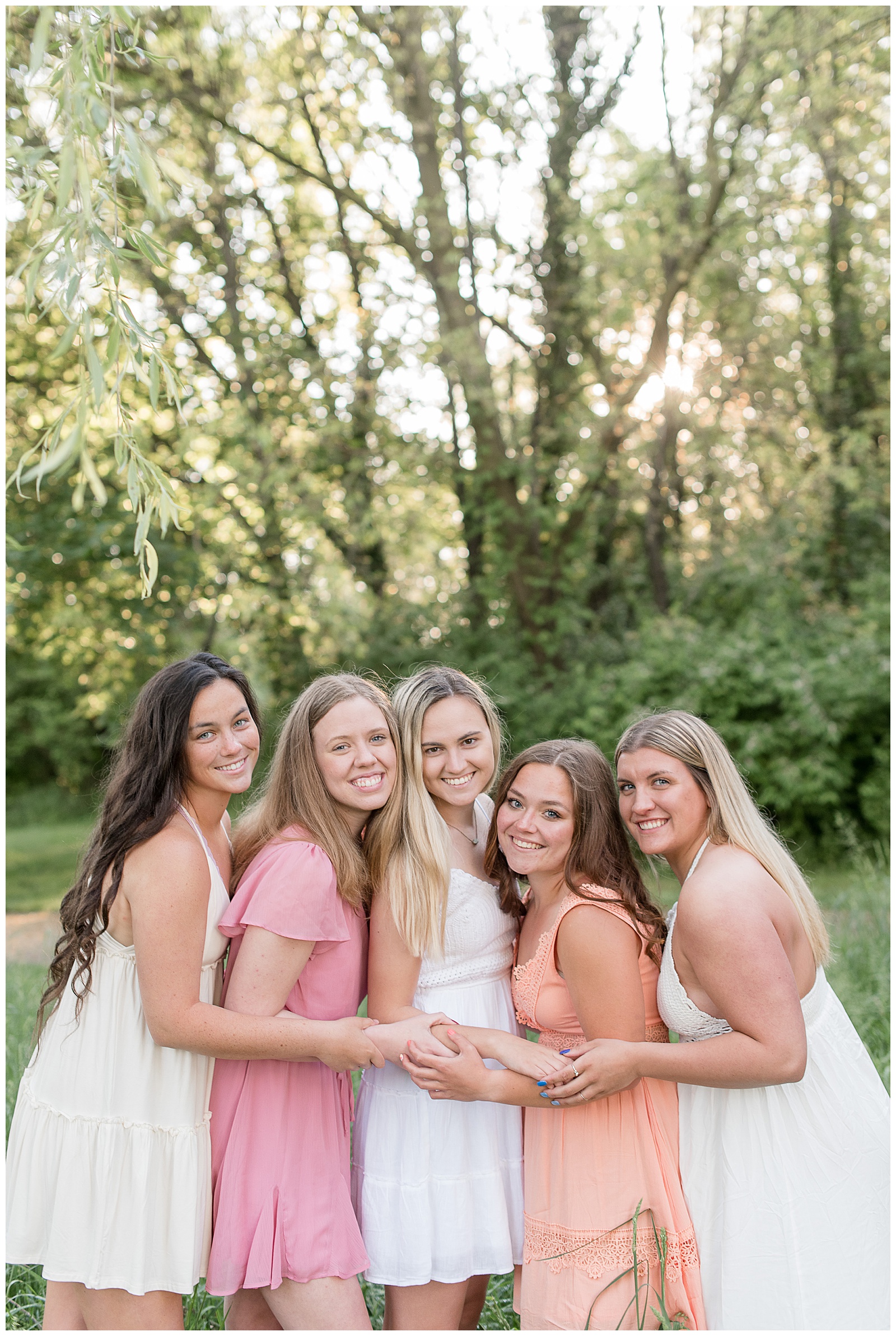 close up of senior girls facing each other holding forearms smiling in front of trees in lancaster pennsylvania