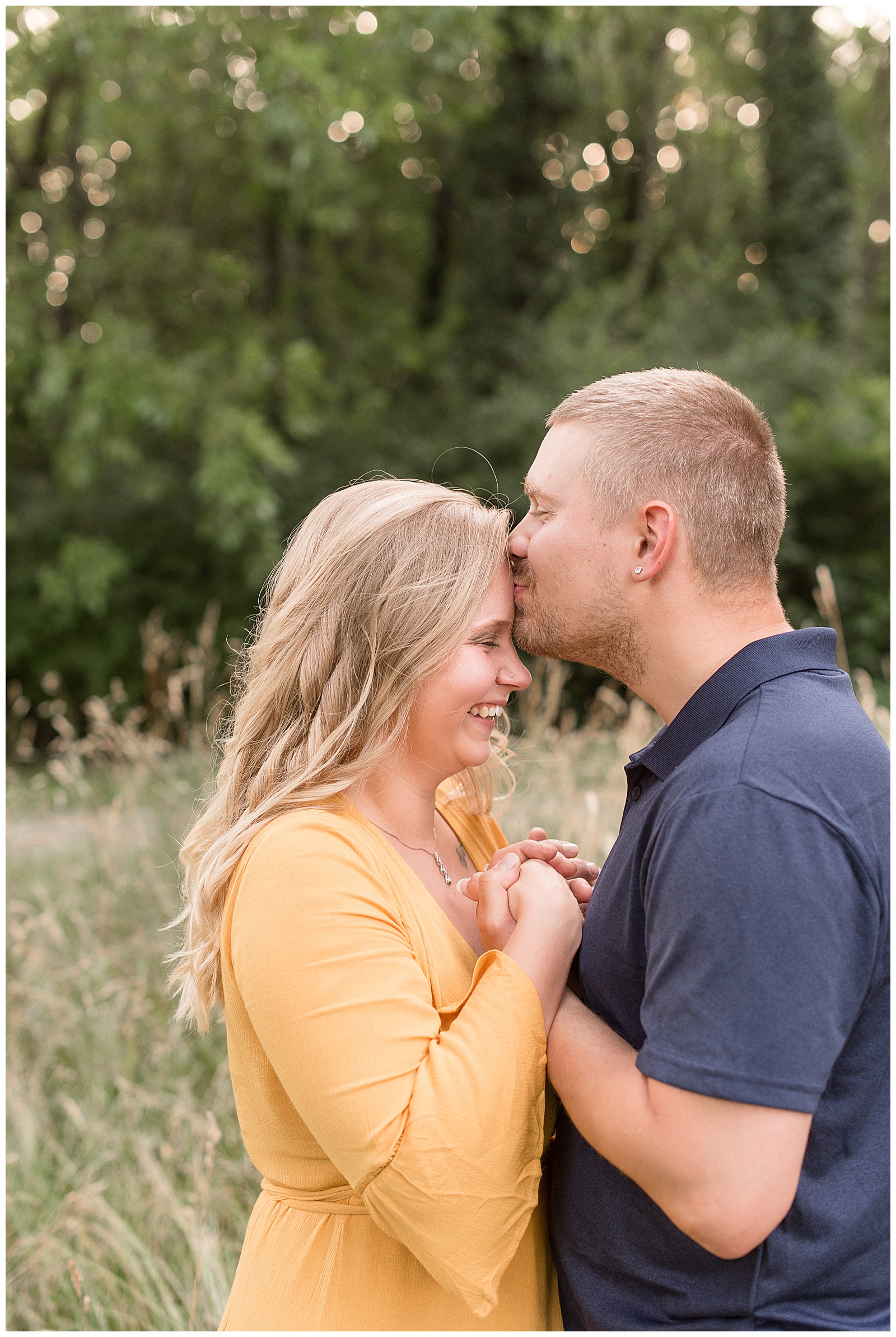 groom-to-be kissing bride-to-be's forehead as she smiles and they hug tightly in tall grasses in lancaster pennsylvania