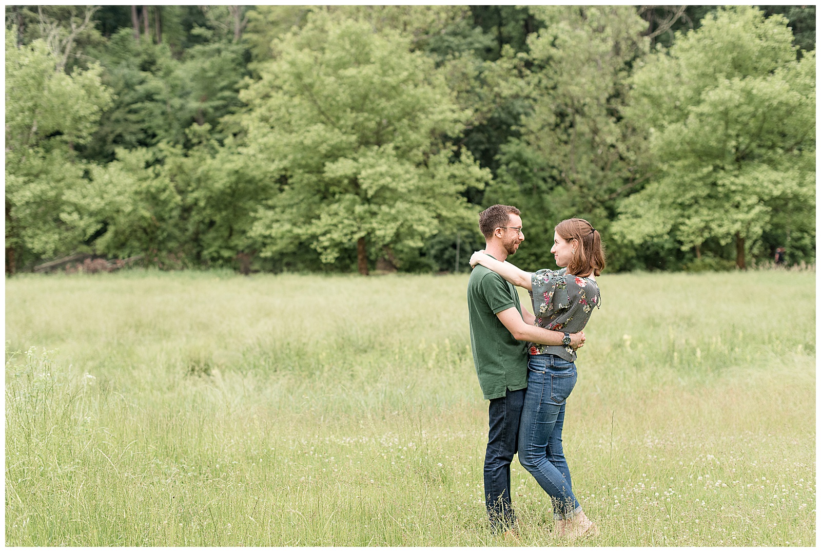 couple in tree lined grass field with their arms wrapped around one another in mechanicsburg, pennsylvania