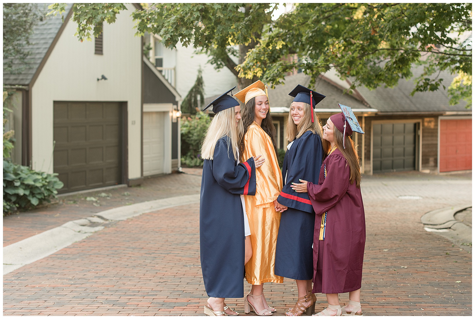 senior girls in caps and gowns huddled together in lancaster city with row of garages behind them