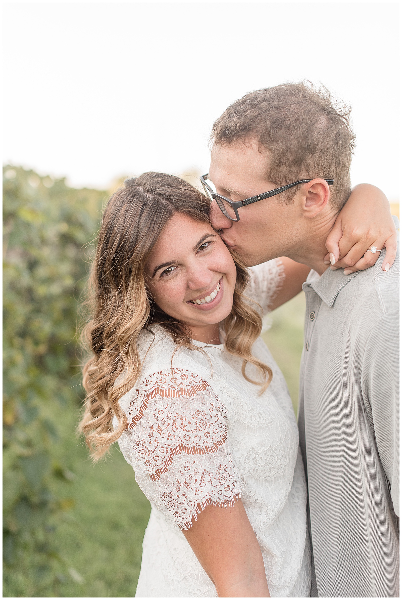 closeup photo of girl smiling as her guy kisses her on the left cheek on bright sunny evening at vineyards at hershey