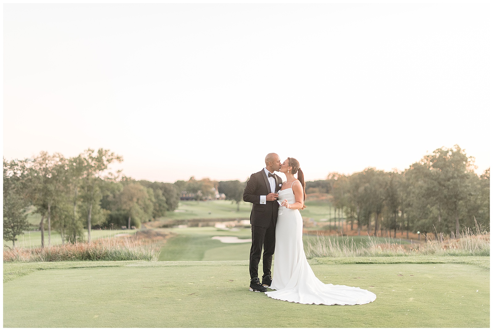 groom and bride kissing on golf course with fairway behind them at north jersey country club
