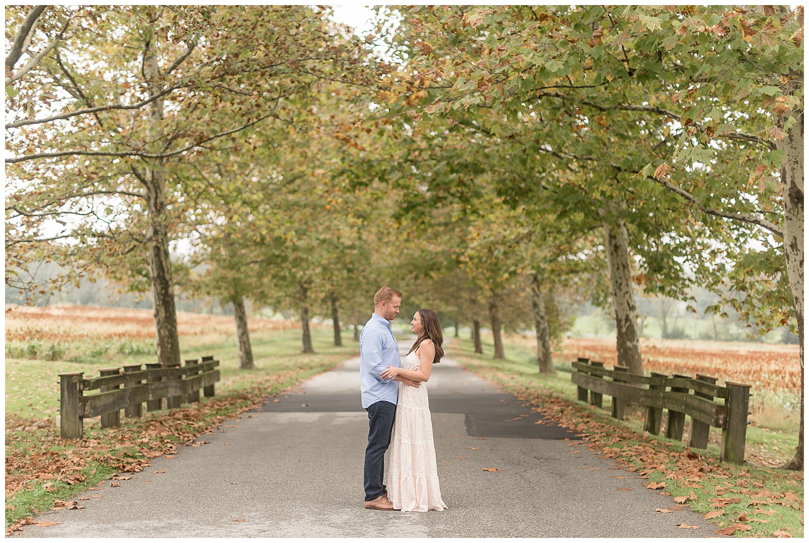 engaged couple facing each other and smiling as they standing in center of tree-lined stone pathway at springton manor farm in chester county pennsylvania