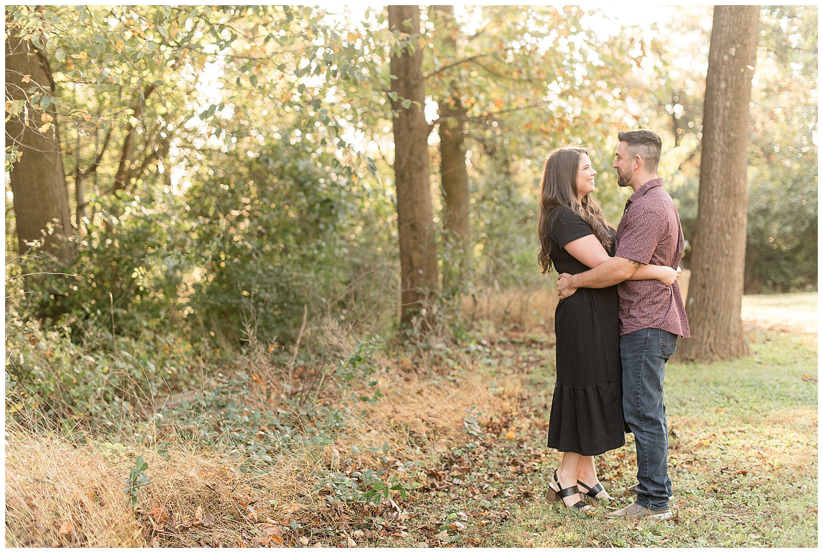 engaged couple hugging tightly on right side of photo with colorful fall trees behind them at pinnacle park in holtwood pennsylvania