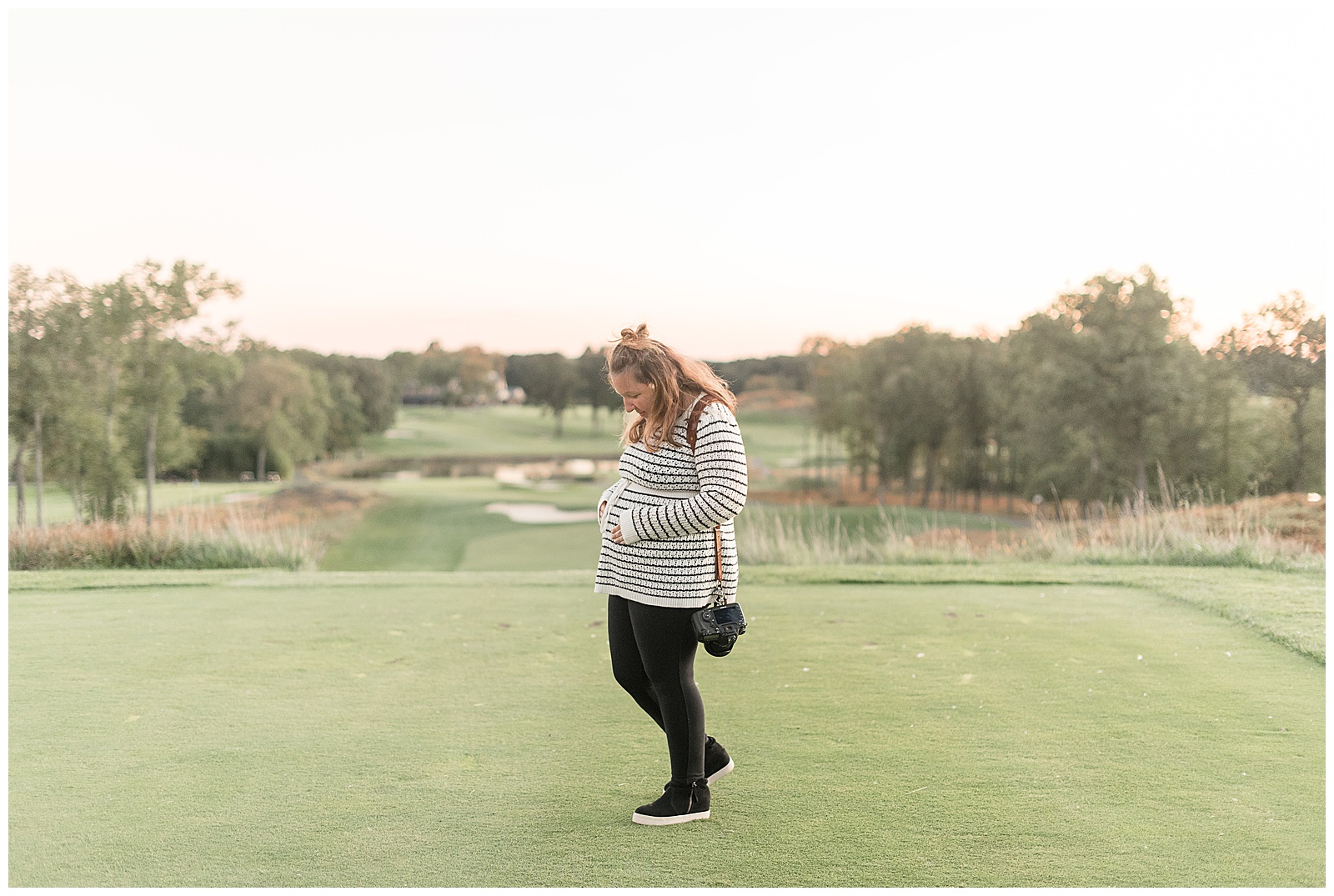 photographer holding her pregnant belly and looking down at it as she stands on golf green at north jersey country club on sunny day
