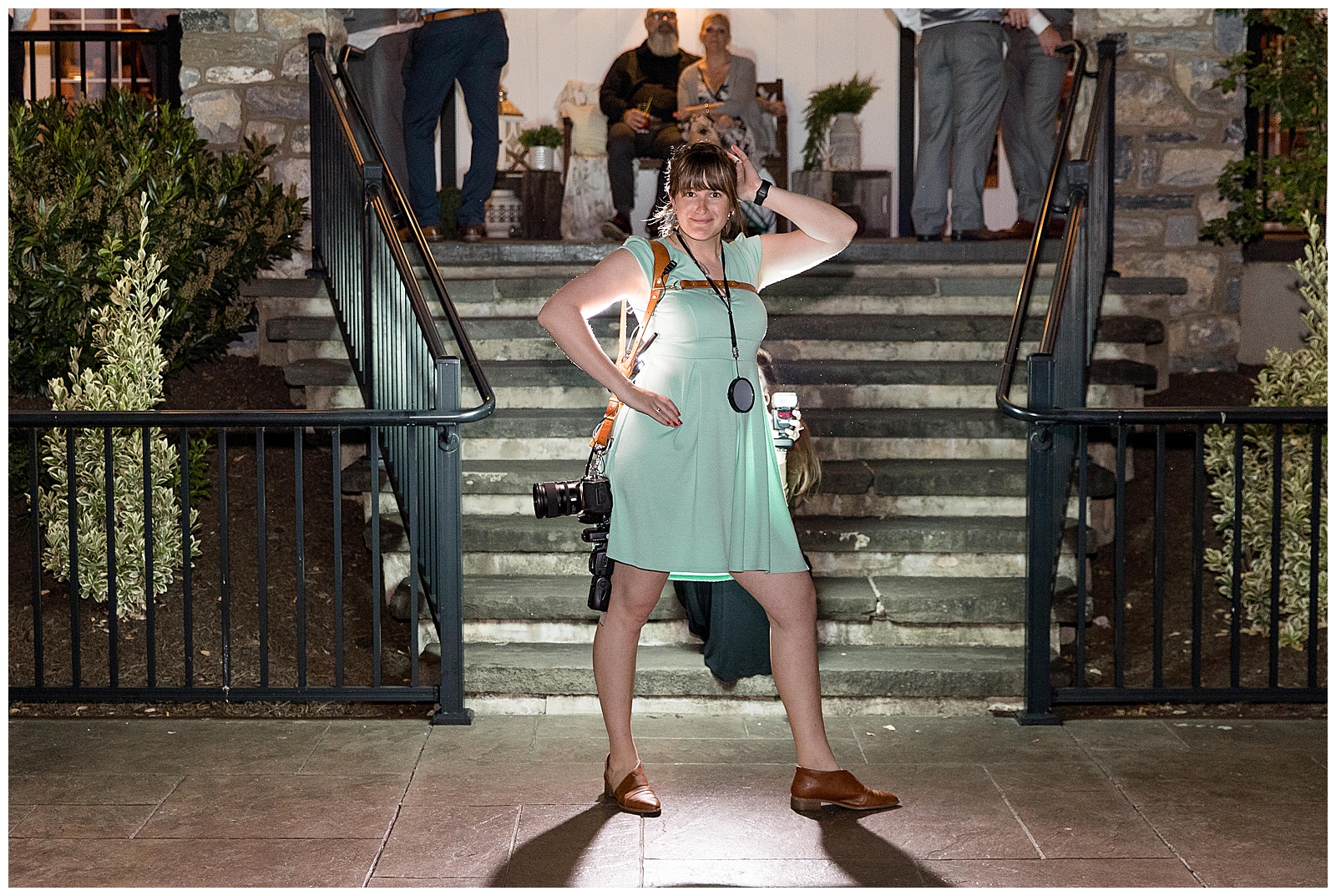 photographer striking a pose with right hand on hip and left hand on head by staircase at reception venue at nighttime