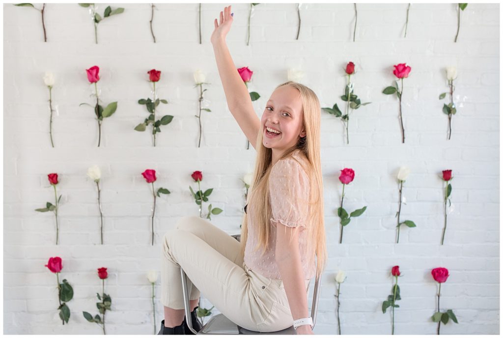 senior girl sitting with left shoulder toward camera and right arm high by rose-covered wall at hingework in lancaster, pennsylvania
