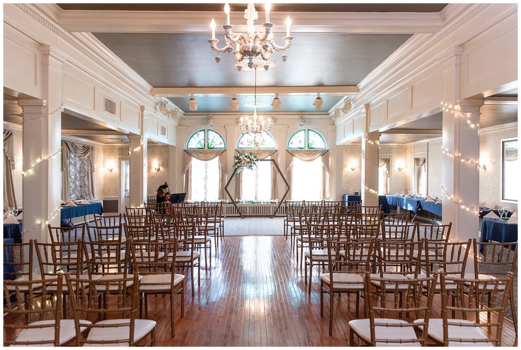 wedding ceremony ballroom with rows of wooden chairs and hexagon floral display by three large windows at the lititz springs inn and spa