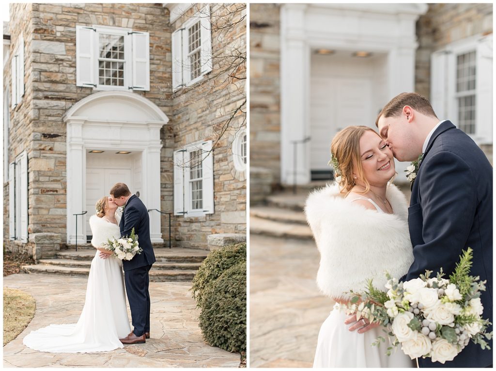 groom kissing his bride on her left cheek as she smiles on cold winter day by gray stone building