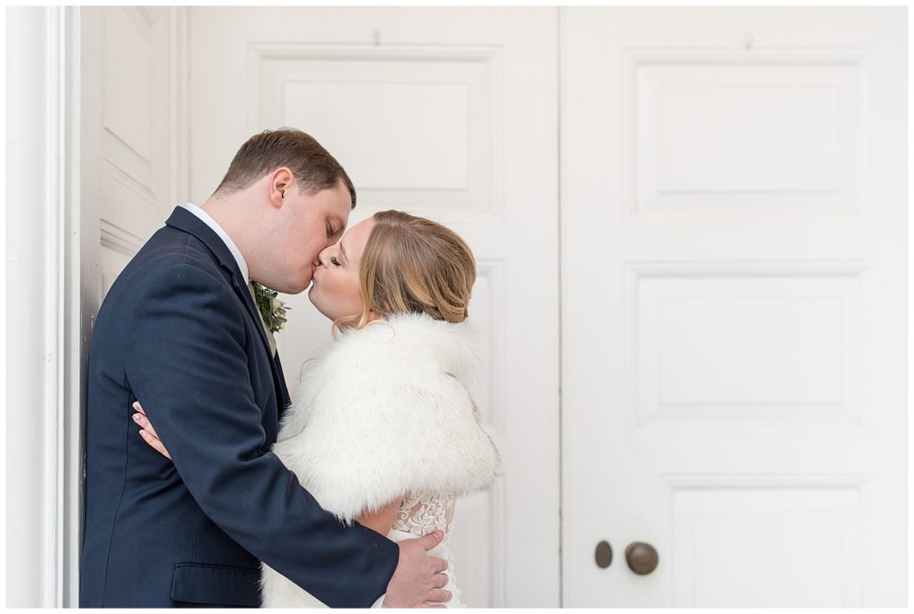 groom hugging his bride as they kiss in front of white doors in downtown lititz pennsylvania