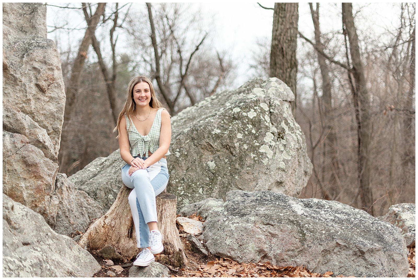 senior girl sitting on large rock in tank top and jeans on winter day at samuel lewis state park