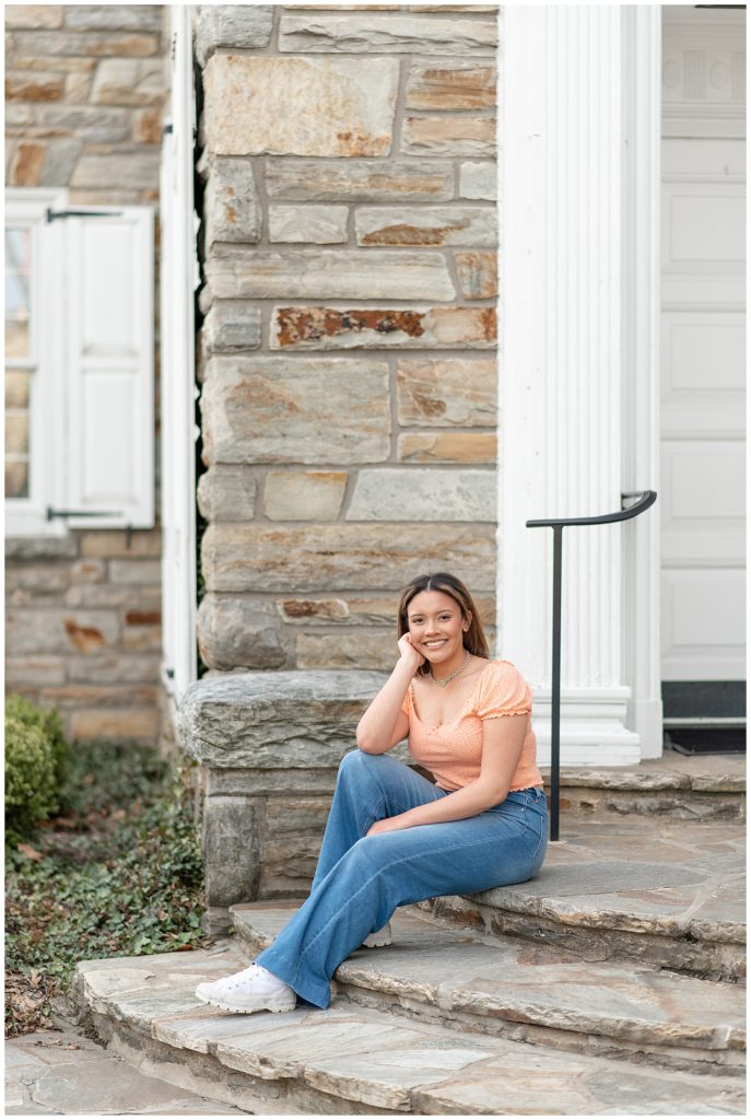 senior girl sitting on steps of historical building with her right elbow on her right knee in lititz, pennsylvania