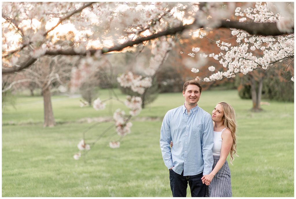 girl holding onto guy's left hand as she looks up at him under cherry blossom in lancaster, pennsylvania