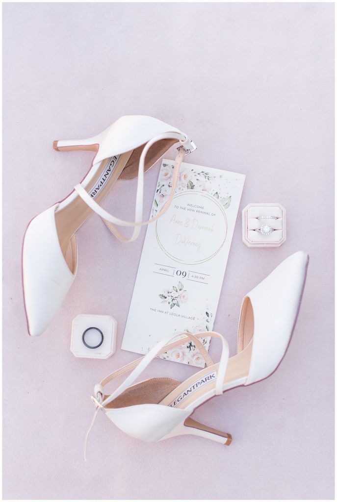 bride's strappy white high heels displayed with wedding invitation and rings on light pink background in leola, pennsylvania