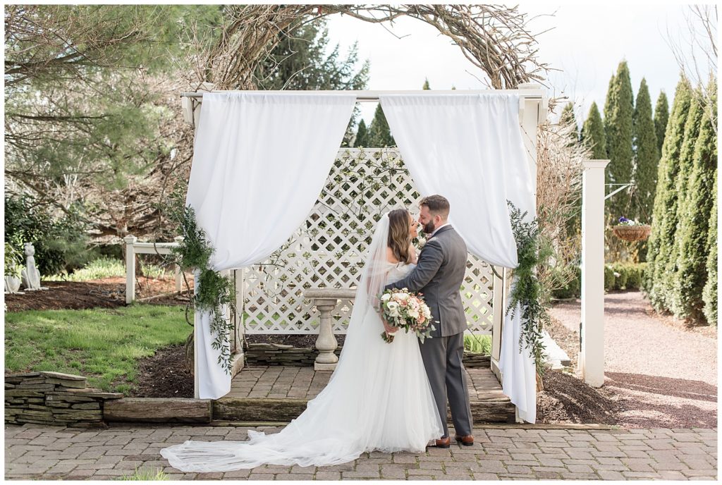 bride and groom standing close together by outdoor display with white curtains in leola, pennsylvania