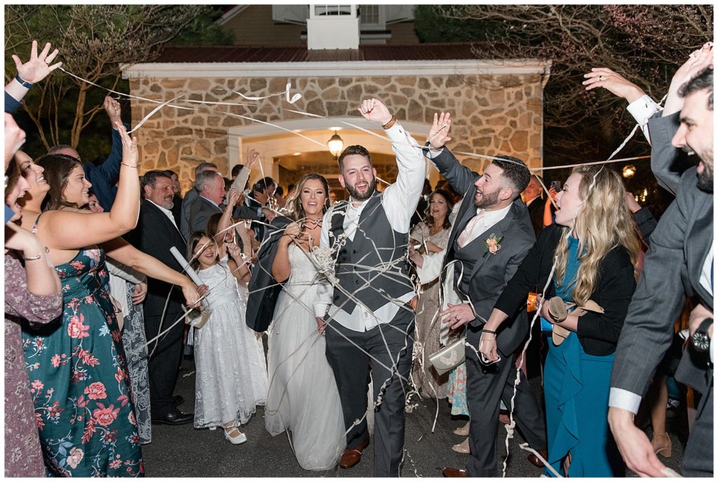 bride and groom leaving their reception through streamers at nighttime as guests cheer in leola, pennsylvania