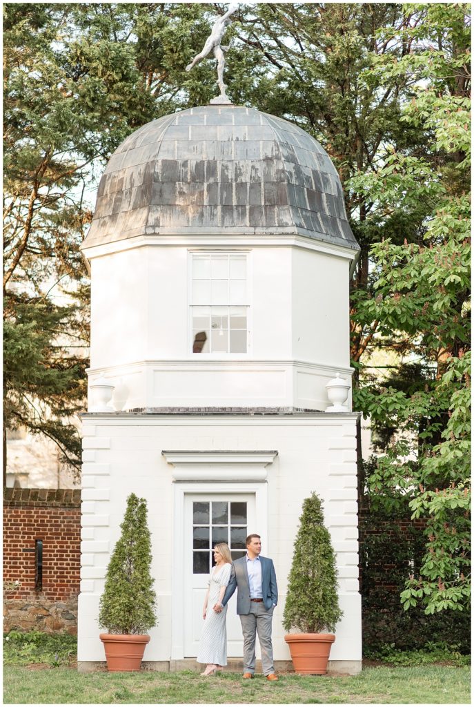 engaged couple standing by historic white tower at the paca house and gardens in annapolis maryland