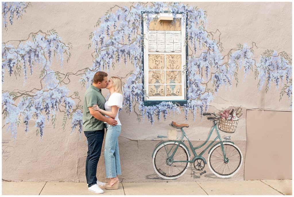 engaged couple kissing by wall painted with flowers and a bicycle in annapolis maryland