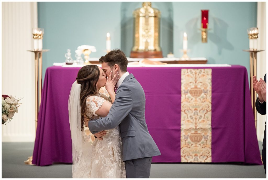 bride and groom sharing their first kiss during wedding ceremony inside beautiful catholic church in central pennsylvania