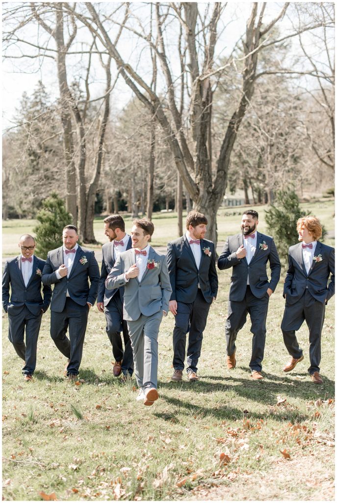 groom walking slightly ahead of his groomsmen in candid photo outside at stock's manor