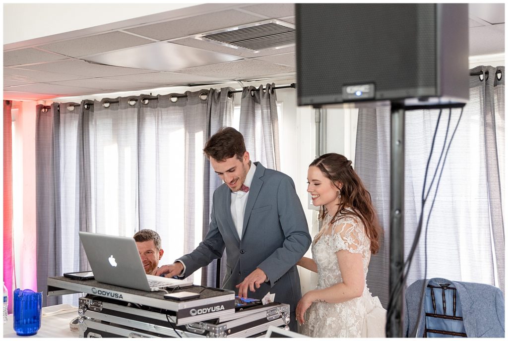 groom behind the dj's table with this bride by his side as they select a song during their reception at stock's manor