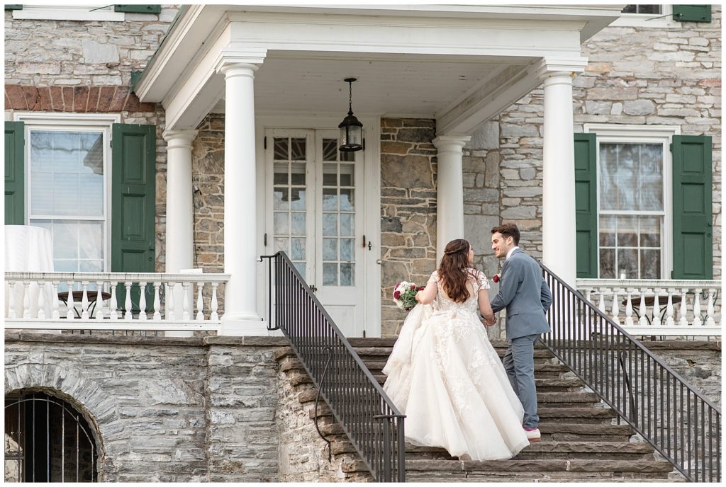 bride and groom holding hands as they walk up stairs of porch to historic home at stock's manor in mechanicsburg, pennsylvania