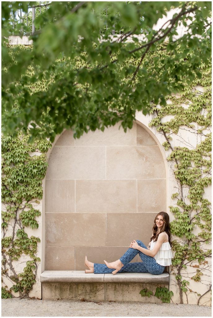 senior girl sitting on concrete bench with legs extended under ivy archway at masonic village