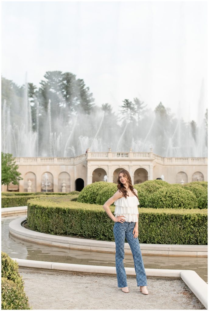 senior girl with right hand on hip standing by beautifully landscaped garden and fountains at masonic village