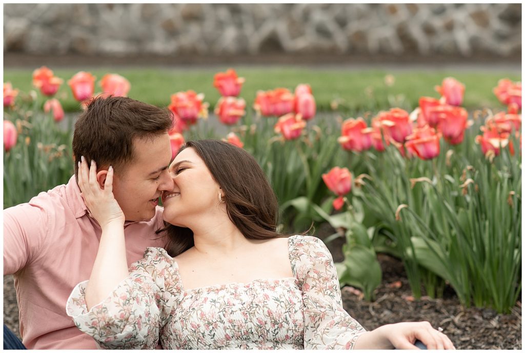 girl leaning back to kiss guy as they sit in front of blooming tulips at masonic village