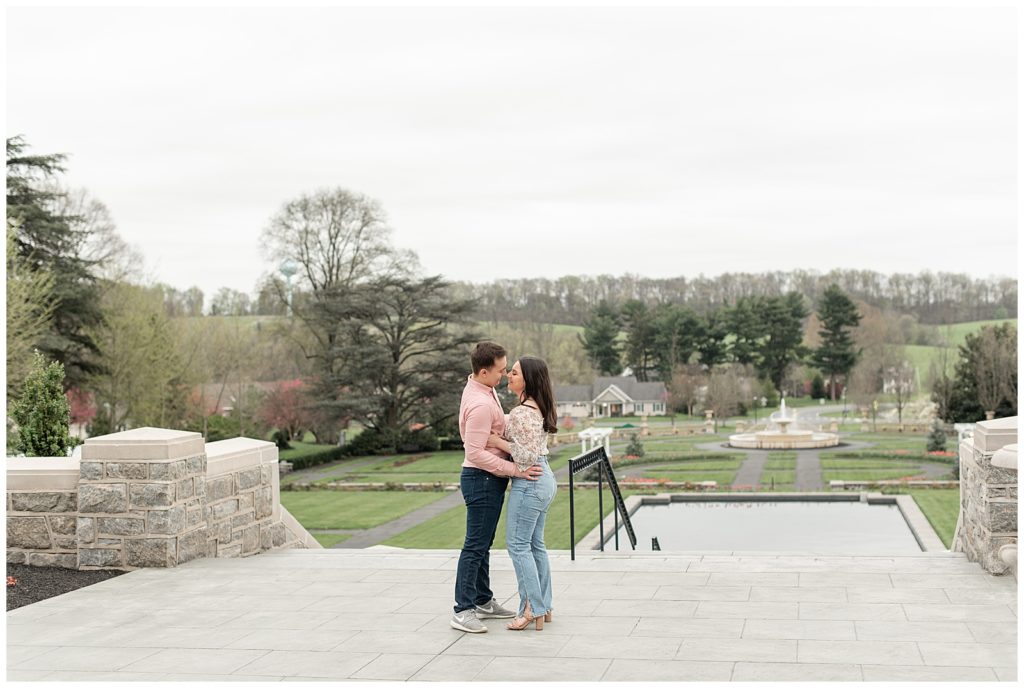 engaged couple almost kissing atop concrete steps overlooking lawn at masonic village