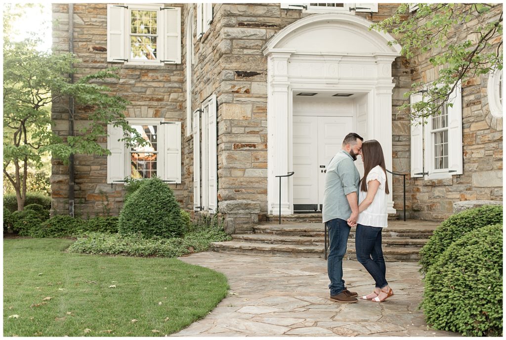 engaged couple holding hands and touching their foreheads together by historic stone building in downtown lititz