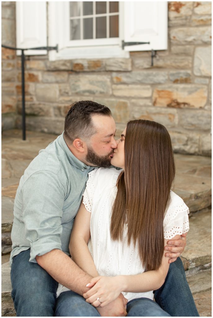 close up photo of engaged couple kissing while sitting on steps of historic stone building in lancaster county pennsylvania