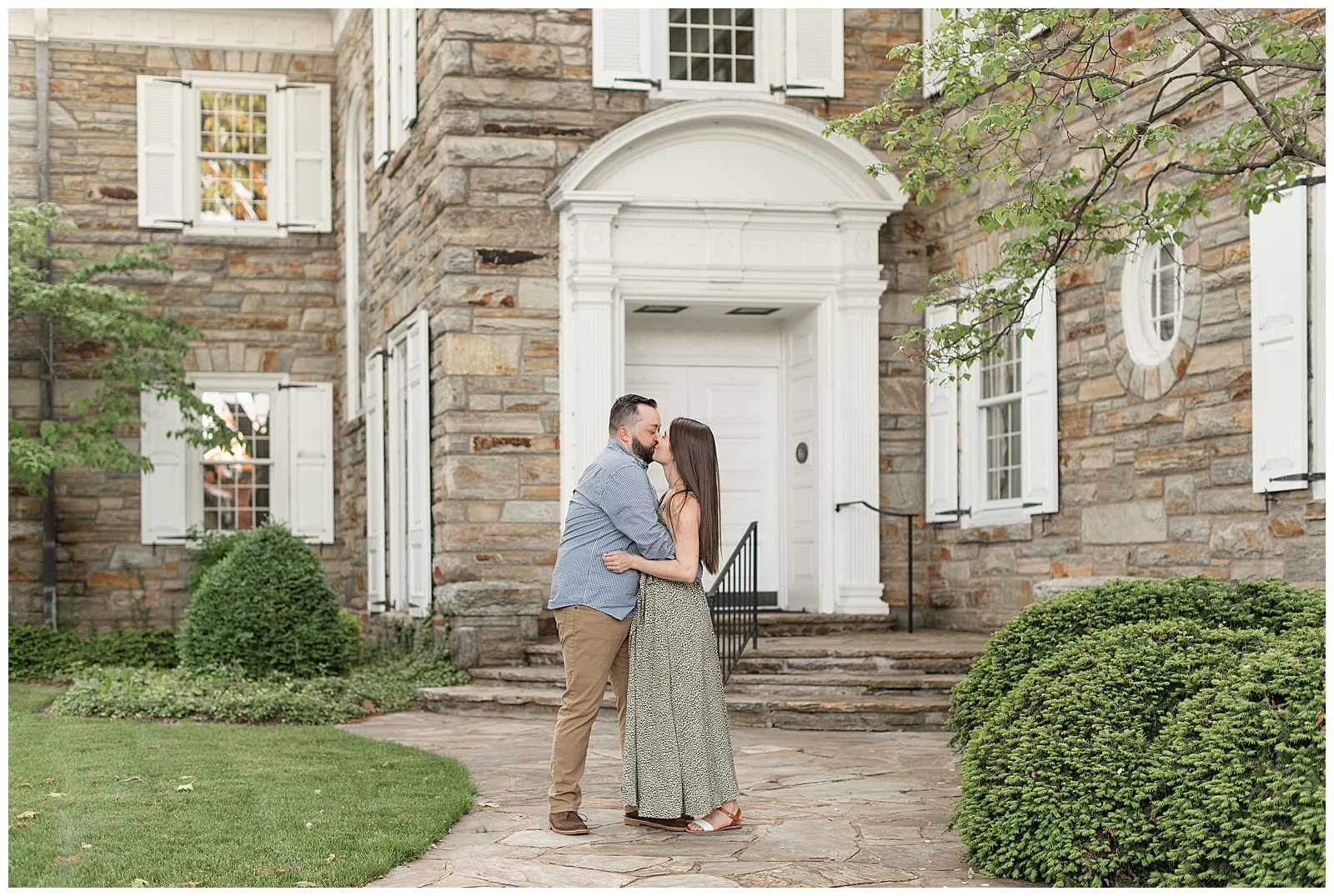 engaged couple hugging and kissing on stone pathway by historic stone building in lititz pennsylvania