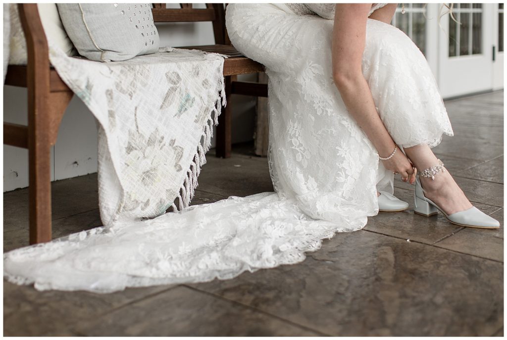 bride's long dress train draped on the floor as she bends down to buckle her shoe in lancaster pa