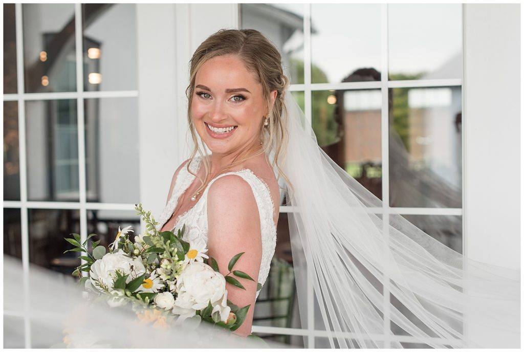 bride smiling as she holds her bouquet of white flowers and daisies at the barn at silverstone