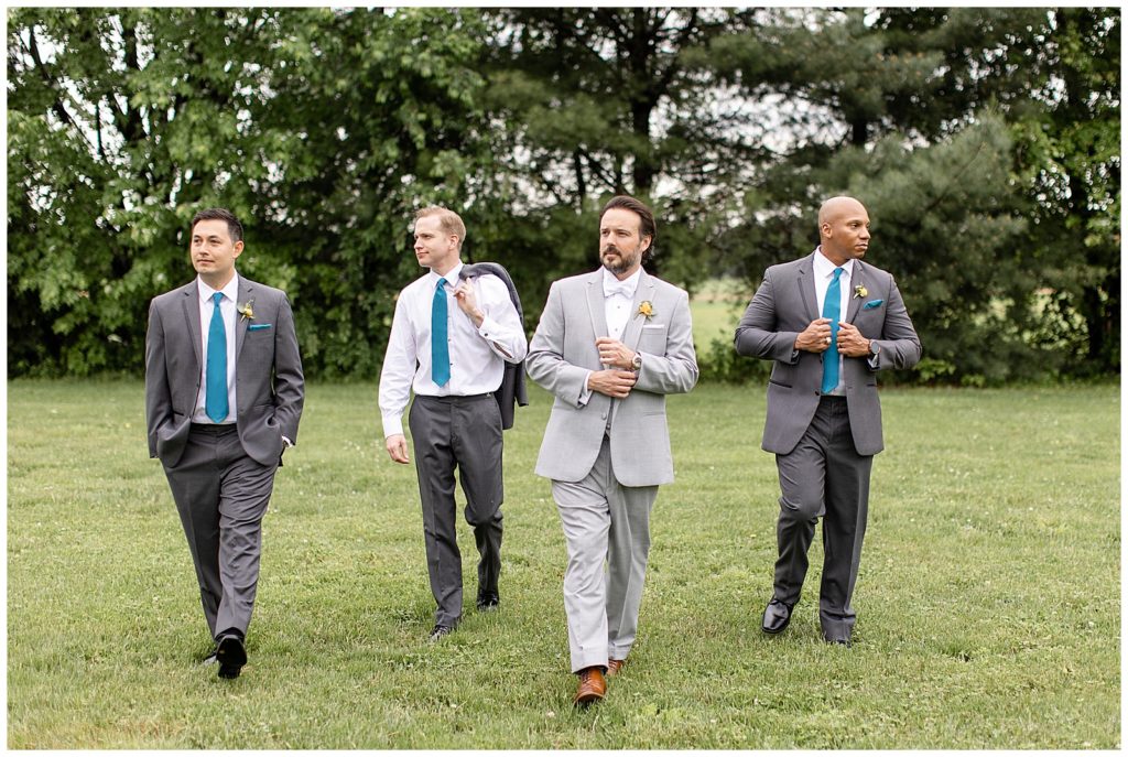 groom and groomsmen walking toward camera looking in opposite directions in grass at the barn at silverstone
