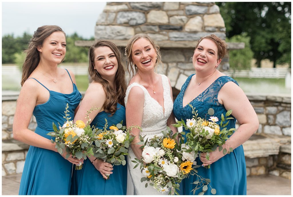 bride and bridesmaids all huddled together smiling by stone outdoor fireplace in lancaster pennsylvania