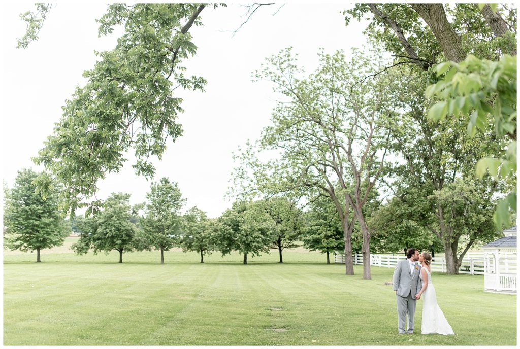 couple is kissing in huge grass lawn and row of trees and standing on right side of photo in lancaster county
