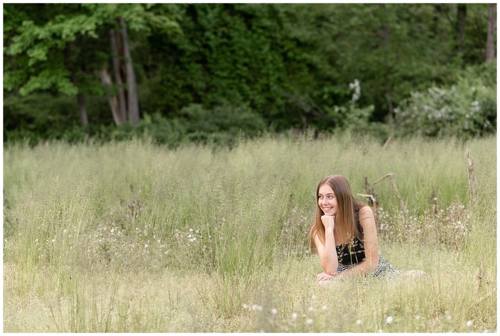 senior girl wearing black tank top and black and white skirt sitting in grassy meadow looking right with chin on right hand in lancaster pa