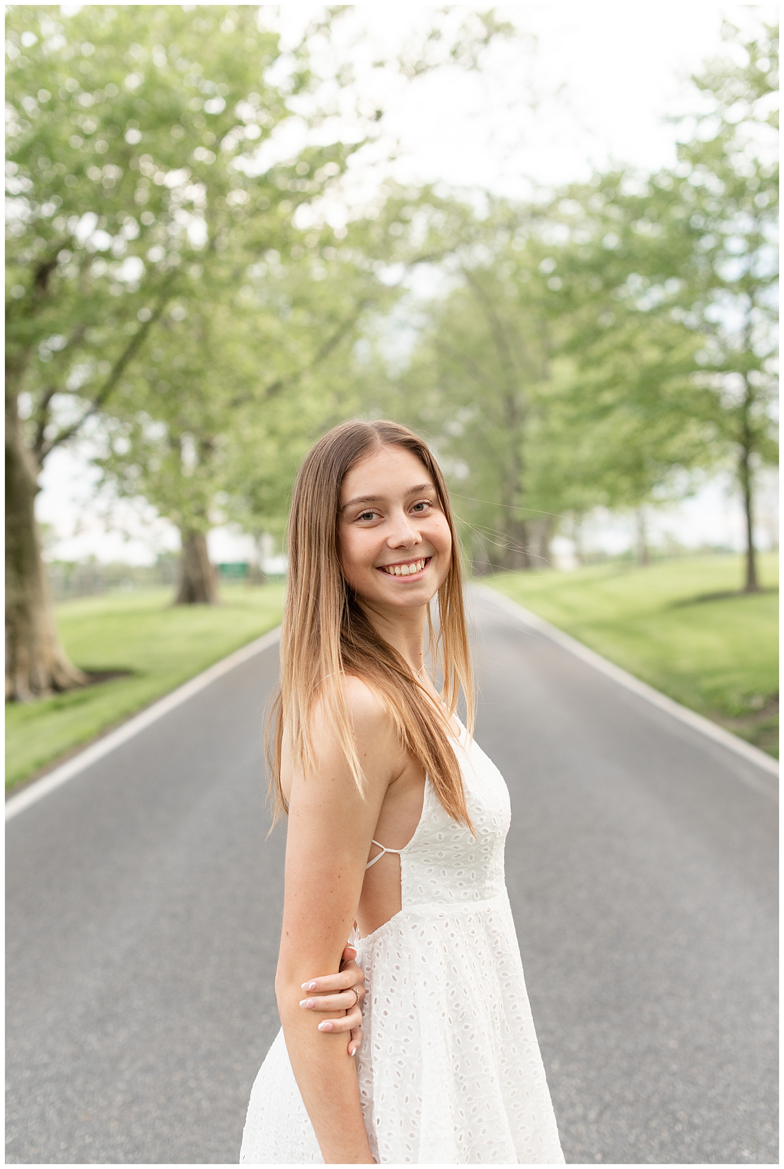 senior girl standing in middle of tree-lined driveway with right shoulder toward camera in lancaster county