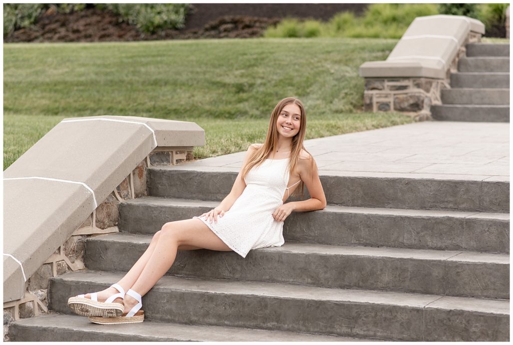 senior girl leaning back on steps looking left and smiling big on sunny evening at masonic village