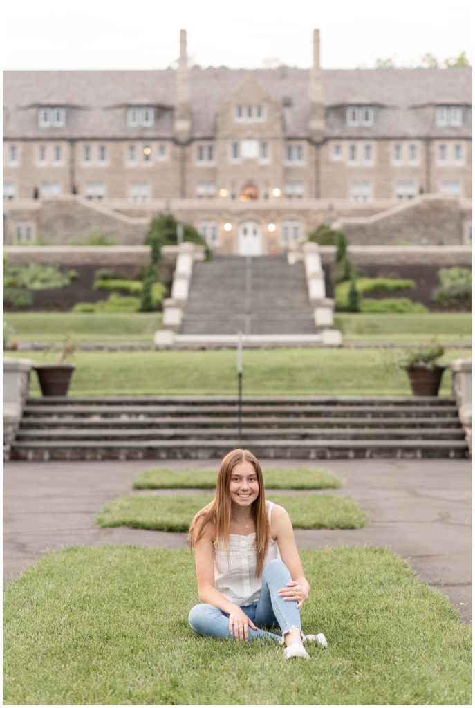 senior girl sitting in manicured lawn with huge building behind her at masonic village in elizabethtown pennsylvania