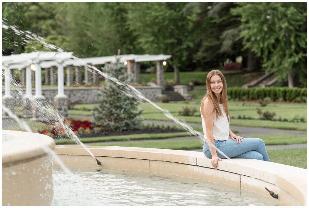 senior girl sitting along concrete edge of fountain looking over right shoulder at masonic village in lancaster pennsylvania