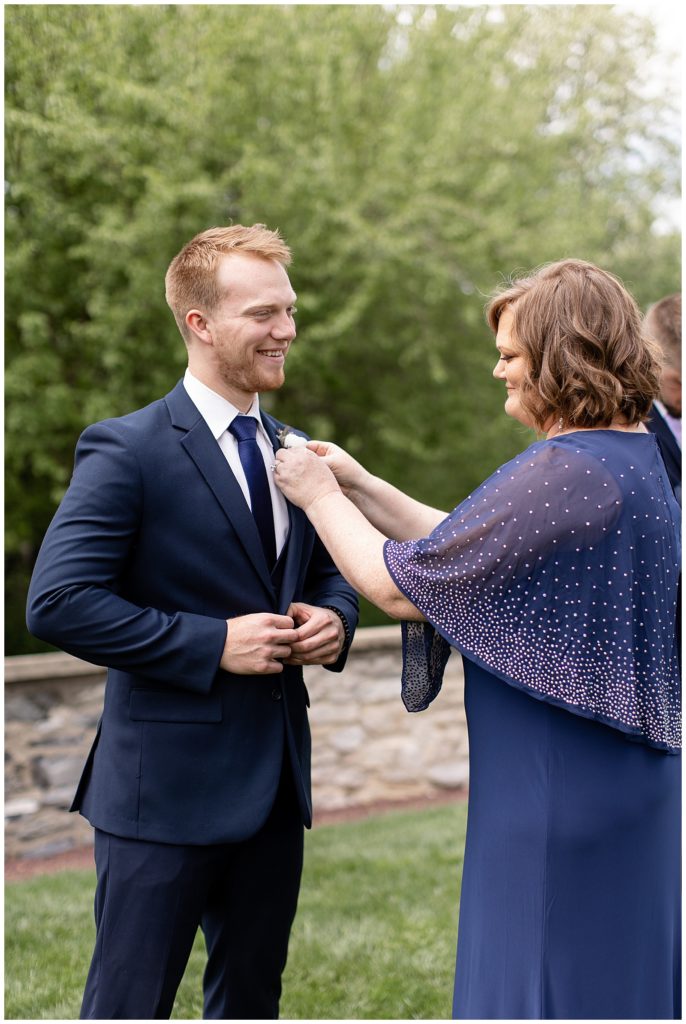 mother of the groom helping pin boutonnière on her son's navy blue jacket at melhorn manor