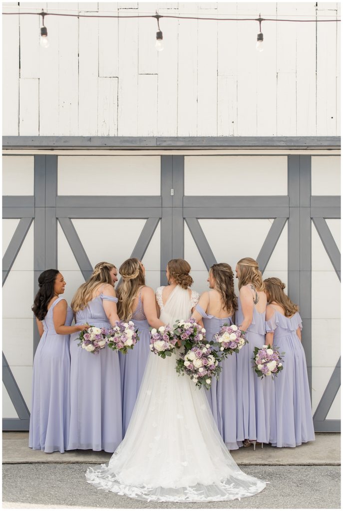 brides and bridesmaids with backs toward camera and bouquets around each other by barn doors in lancaster county pennsylvania