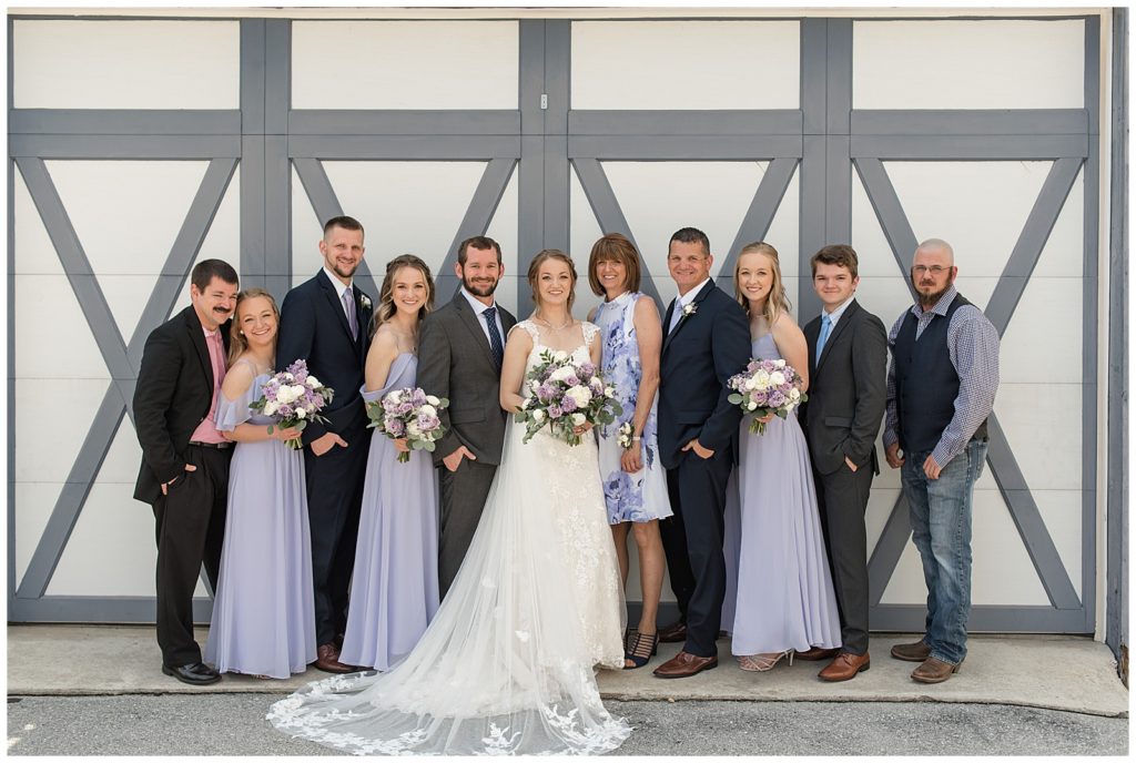 bride and groom with the bride's family by barn door at melhorn manor on sunny spring day