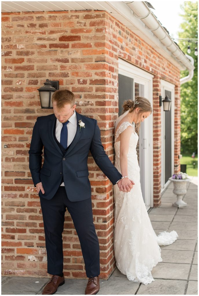 groom and bride holding hands around corner of brick building and anticipating their first look at melhorn manor
