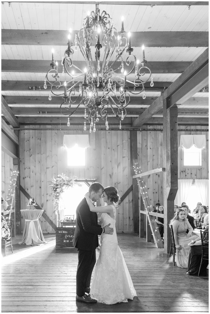 black and white photo of couple sharing their first dance under chandelier inside barn at melhorn manor