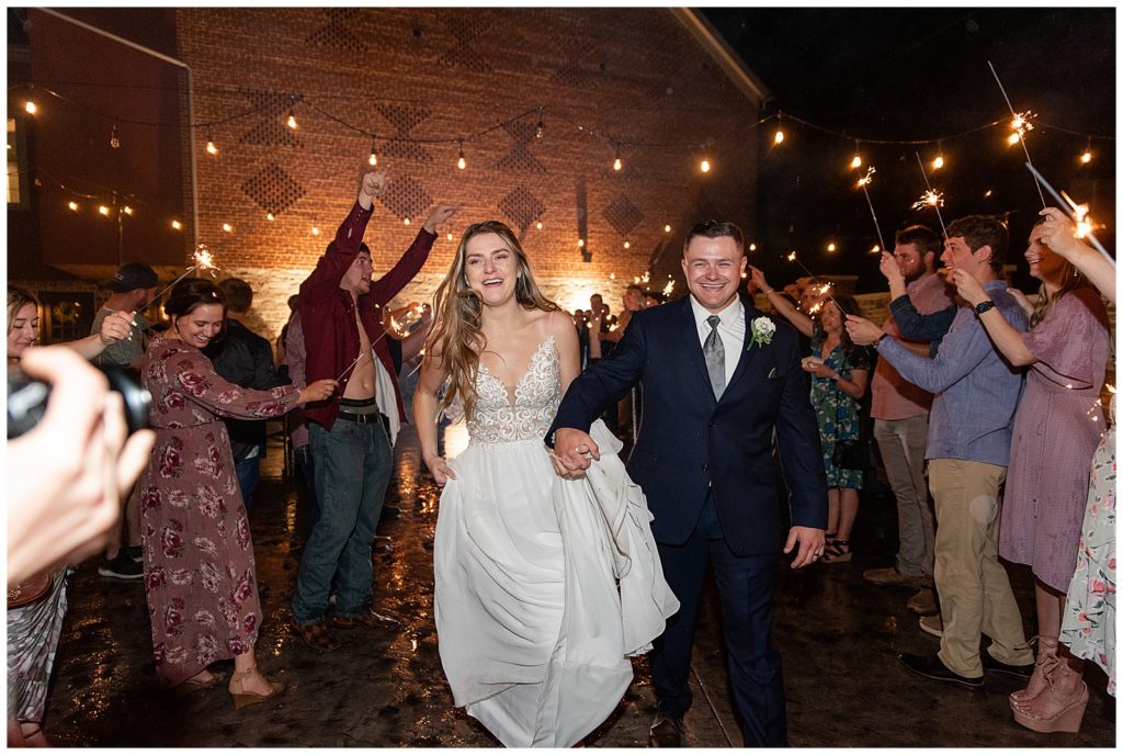 bride and groom holding hands as they run through aisle of guests toward camera leaving their reception at brick gables