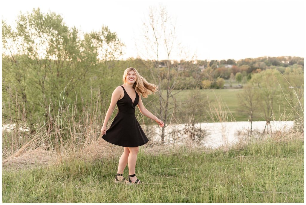senior girl in black dress twirling by tall grasses and pond at sunset at manheim township park in lancaster county